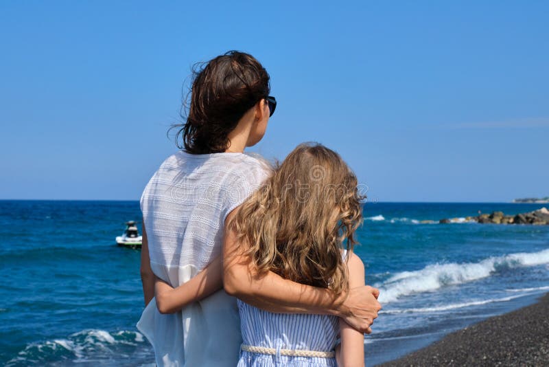 Lycklig mamma och dotter som kramar och går tillsammans längs strandbänken arkivbild