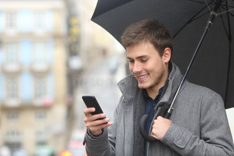 Lycklig man som kontrollerar telefonen under ett paraply i vinter royaltyfri fotografi Lycklig man som kontrollerar telefonen under ett paraply i vinter royaltyfri fotografi