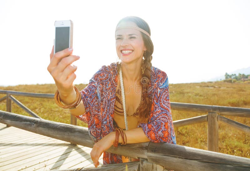 Lycklig modebohoflicka utomhus med smartphonen som tar selfie arkivfoton Lycklig modebohoflicka utomhus med smartphonen som tar selfie arkivfoton
