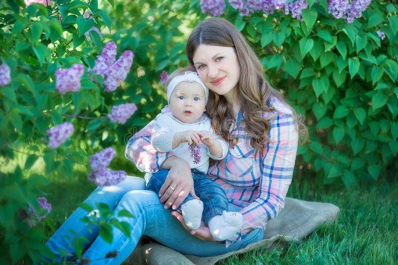 Lycklig moder och dotter med gröna äpplen i trädgården av blommande lilor royaltyfri foto Lycklig moder och dotter med gröna äpplen i trädgården av blommande lilor royaltyfri foto