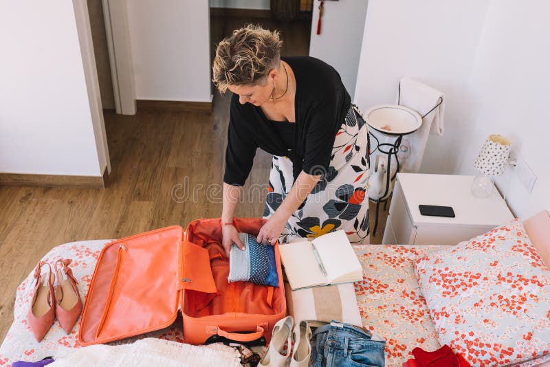 mature woman traveller using a smart phone and packing her suitcase preparing to travel on a summer holiday. Vertical, leisure and holiday concept. Room, illuminated by natural light, suitcase with clothes. mature woman traveller using a smart phone and packing her suitcase preparing to travel on a summer holiday. Vertical, leisure and holiday concept. Room, illuminated by natural light, suitcase with clothes.