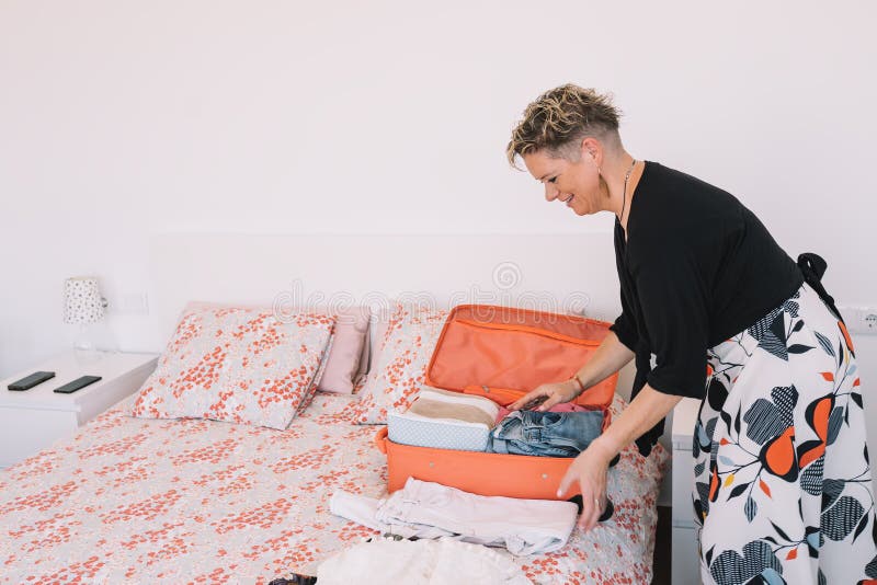 mature woman traveller using a smart phone and packing her suitcase preparing to travel on a summer holiday. leisure and holiday concept. Room, illuminated by natural light, suitcase with clothes. mature woman traveller using a smart phone and packing her suitcase preparing to travel on a summer holiday. leisure and holiday concept. Room, illuminated by natural light, suitcase with clothes.