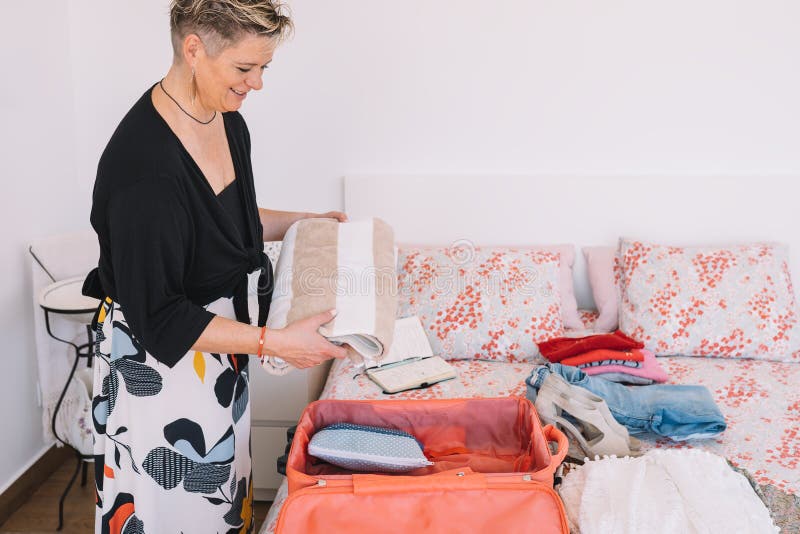 mature woman traveller using a smart phone and packing her suitcase preparing to travel on a summer holiday. leisure and holiday concept. Room, illuminated by natural light, suitcase with clothes. mature woman traveller using a smart phone and packing her suitcase preparing to travel on a summer holiday. leisure and holiday concept. Room, illuminated by natural light, suitcase with clothes.