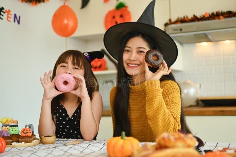 Lycklig mor och liten söt dotter som äter utsökt munk under halloween-firandet arkivbild