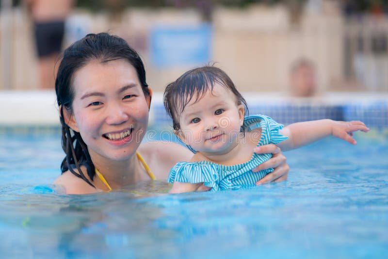 Lycklig och vacker asiatisk kvinna som håller sin lilla flicka, som leker koreansk mor och ädel dotter som leker på vatten på fotografering för bildbyråer