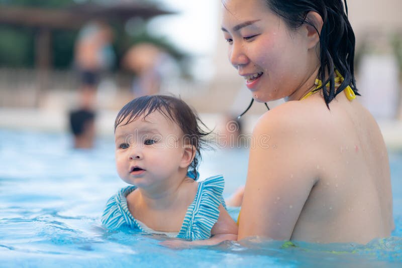 Lycklig och vacker asiatisk kvinna som håller sin lilla flicka, som leker koreansk mor och ädel dotter som leker på vatten på royaltyfria bilder