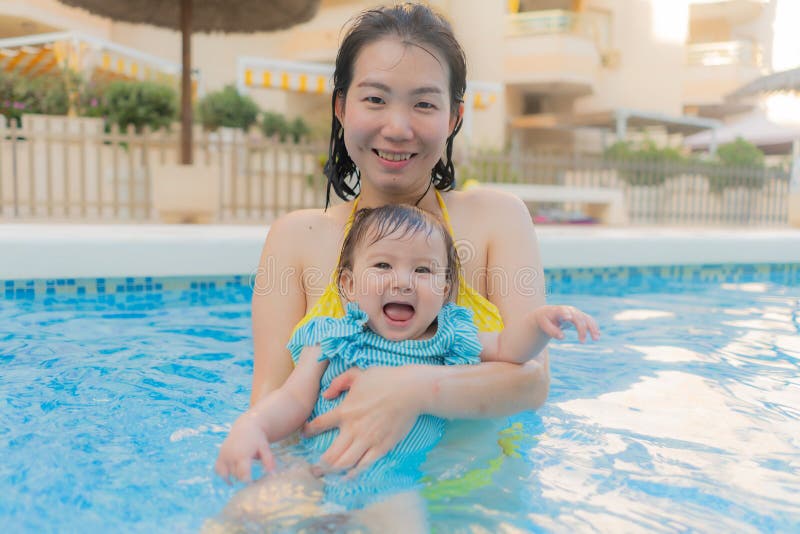 Lycklig och vacker asiatisk kvinna som håller sin lilla flicka, som leker koreansk mor och ädel dotter som leker på vatten på fotografering för bildbyråer