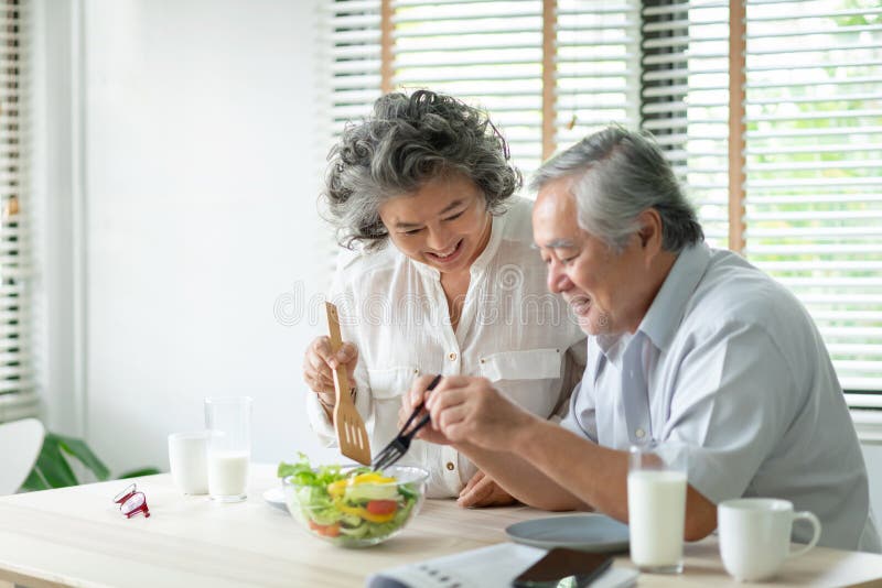 Happy Asian Older couple relaxing preparing and cooking healthy salad at home together. Romantic Senior men and women smiling enjoying a meal. Happy Asian Older couple relaxing preparing and cooking healthy salad at home together. Romantic Senior men and women smiling enjoying a meal