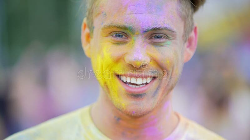 Lycklig stilig man som ler till kameran som tycker om atmosfär på färgfestivalen