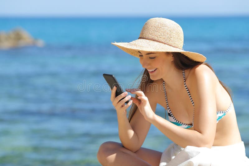 Lycklig sunbather som använder den smarta telefonen på stranden arkivfoton Lycklig sunbather som använder den smarta telefonen på stranden arkivfoton