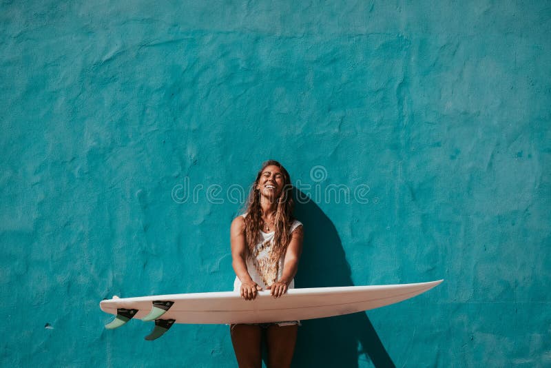Lycklig surfareflicka med surfingbrädan som är främst av den blåa väggen