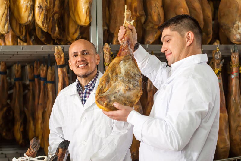 Lycklig teknolog med slaktaren som kontrollerar uttorkningwurst och jamon arkivfoto Lycklig teknolog med slaktaren som kontrollerar uttorkningwurst och jamon arkivfoto