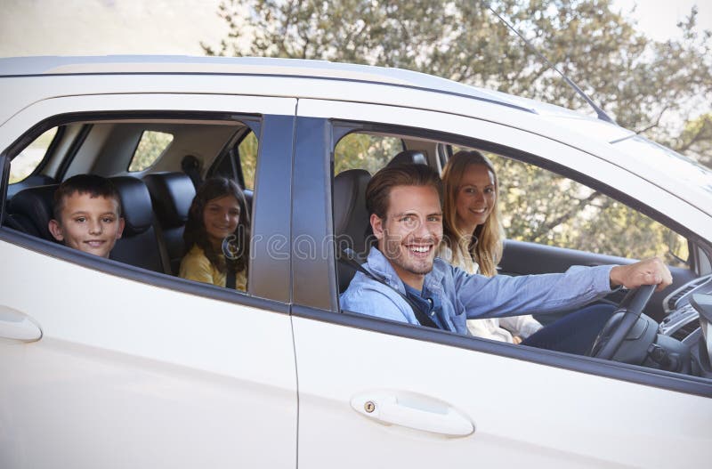 Lycklig ung familj som kör i deras bil som ser till kameran arkivbild