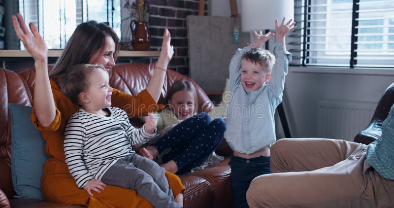 Lycklig ung kaukasisk mor och far går hand i hand med tre barnfamiljer tillsammans med varandra i hemmet för långsam rörelse.