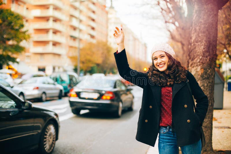 Lycklig ung kvinna som kallar för en taxi i staden arkivbild Lycklig ung kvinna som kallar för en taxi i staden arkivbild