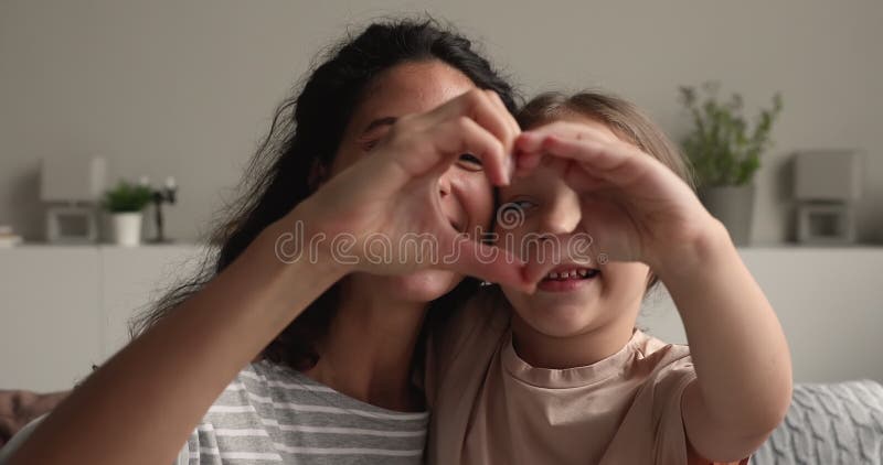 Lycklig ung mor som gör kärleksskylt med leende liten dotter.