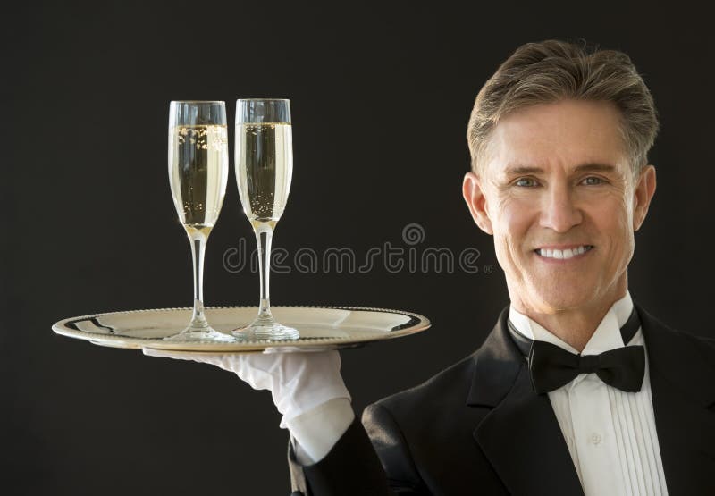 Lycklig uppassare Carrying Serving Tray With Champagne Flutes arkivfoton Lycklig uppassare Carrying Serving Tray With Champagne Flutes arkivfoton