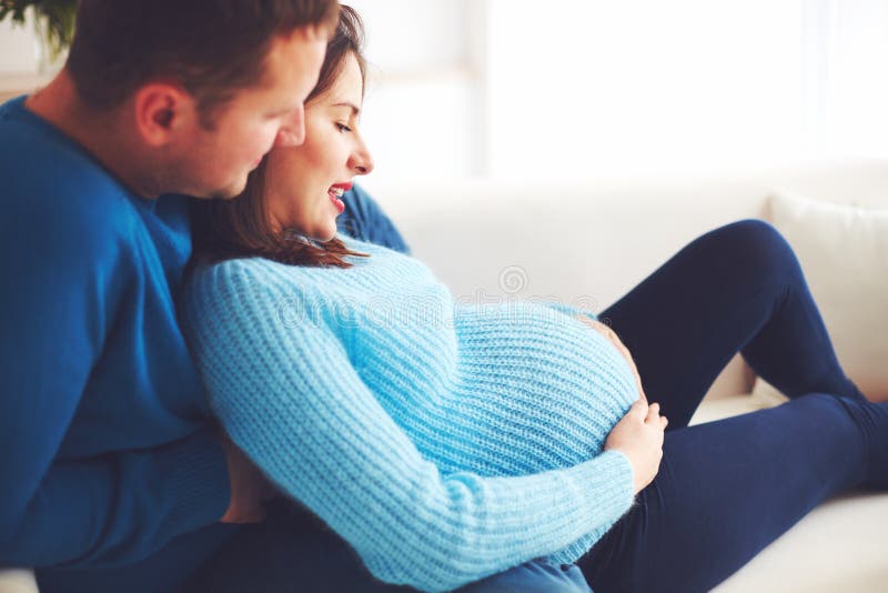 Lyckliga gravida par som hemma kopplar av på soffan