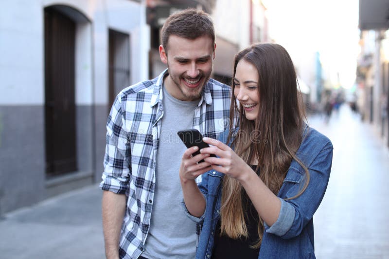 Lyckliga par som går genom att använda mobiltelefonen i gatan fotografering för bildbyråer Lyckliga par som går genom att använda mobiltelefonen i gatan fotografering för bildbyråer
