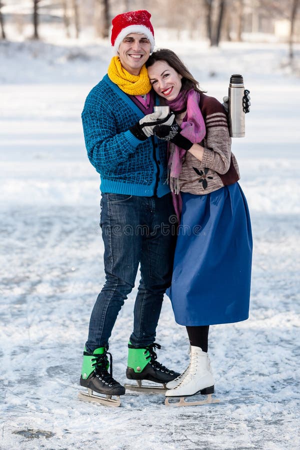 Lyckliga par som har rolig skridskoåkning och dricker varmt te från th royaltyfri bild Lyckliga par som har rolig skridskoåkning och dricker varmt te från th royaltyfri bild