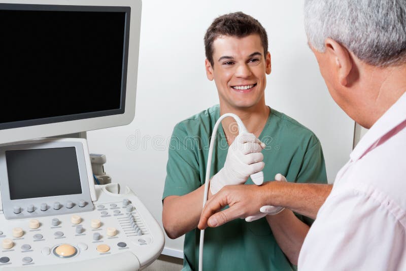 Young male radiologic technician smiling while scanning male patient's hand at clinic. Young male radiologic technician smiling while scanning male patient's hand at clinic