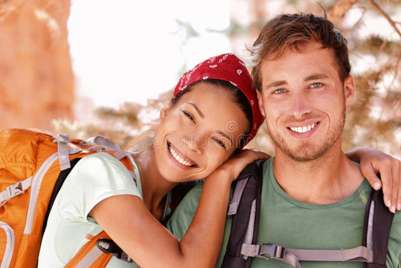 Happy young hikers backpacking on summer travel. Portrait of two friends teenagers or student couple wearing rucksacks bags smiling hiking during road trip vacation or doing volunteering. Happy young hikers backpacking on summer travel. Portrait of two friends teenagers or student couple wearing rucksacks bags smiling hiking during road trip vacation or doing volunteering.