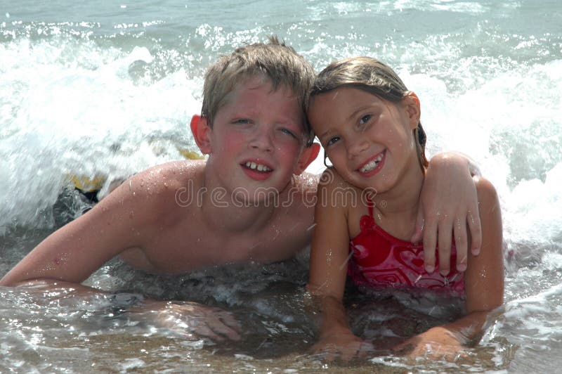 Happy Cousins hang together on vacation on the beach. Boy and girl laying in the ocean waves looking at the camera. Happy Cousins hang together on vacation on the beach. Boy and girl laying in the ocean waves looking at the camera.