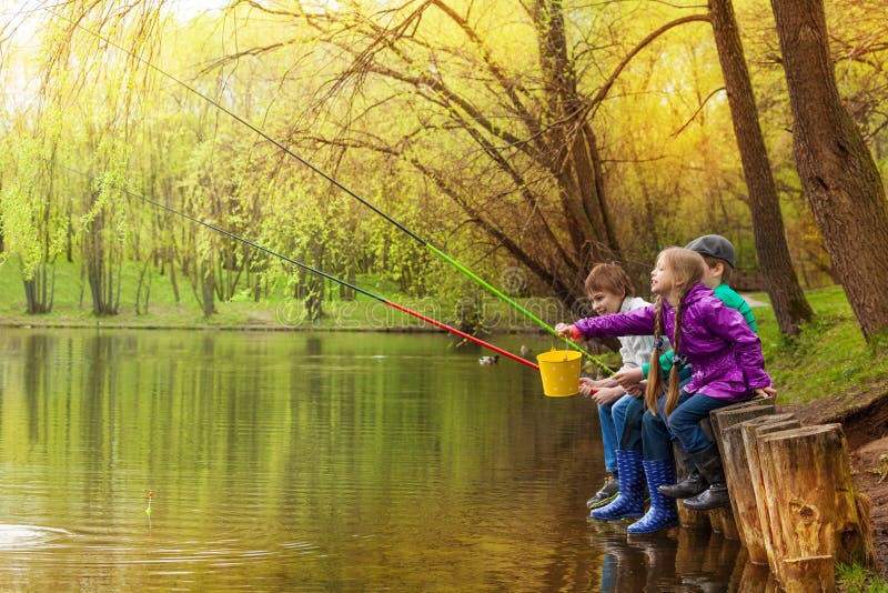 Happy kids sitting and fishing together near the pond with colorful fishing poles in beautiful forest landscape. Happy kids sitting and fishing together near the pond with colorful fishing poles in beautiful forest landscape