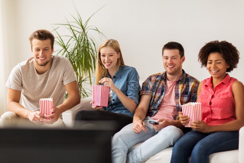 Lyckliga vänner med hållande ögonen på tv för popcorn hemma arkivbild Lyckliga vänner med hållande ögonen på tv för popcorn hemma arkivbild