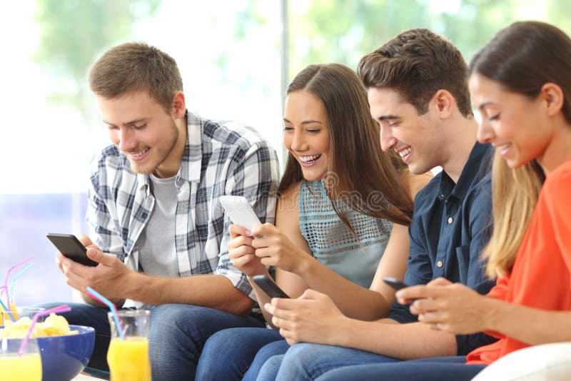 Four happy friends using their mobile phones sitting on a sofa at home with a window in the background. Four happy friends using their mobile phones sitting on a sofa at home with a window in the background