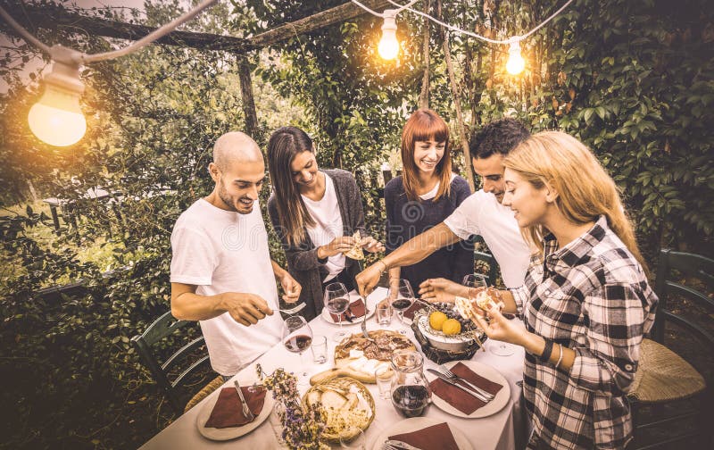 Lyckliga vänner som har gyckel som äter lokal mat på trädgårdpicknickpartiet arkivbild Lyckliga vänner som har gyckel som äter lokal mat på trädgårdpicknickpartiet arkivbild