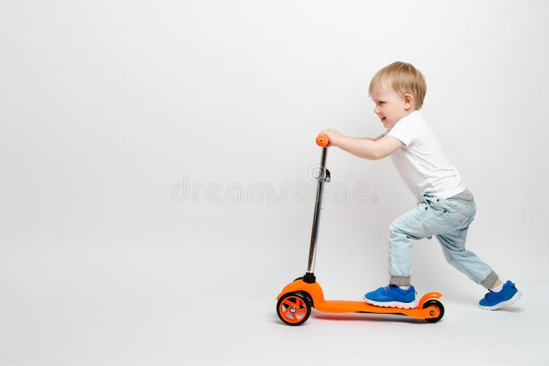 Lyckligt behandla som ett barn lilla barnet i jeans rider en orange sparkcykel på en vit bakgrund i studion royaltyfri foto Lyckligt behandla som ett barn lilla barnet i jeans rider en orange sparkcykel på en vit bakgrund i studion royaltyfri foto
