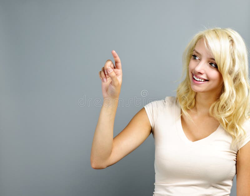 Smiling blonde caucasian woman pointing to the side on grey background. Smiling blonde caucasian woman pointing to the side on grey background