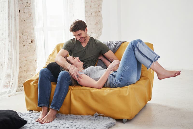 Lying on the boyfriend`s legs. Happy couple relaxing on the yellow sofa in the living room of their new house royalty free stock photography