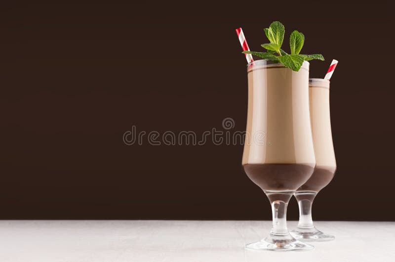 Lyxig milkshake för söt choklad i vinglas med den nya gröna mintkaramellen och rött randigt sugrör på mörk brun bakgrund, royaltyfri foto Lyxig milkshake för söt choklad i vinglas med den nya gröna mintkaramellen och rött randigt sugrör på mörk brun bakgrund, royaltyfri foto