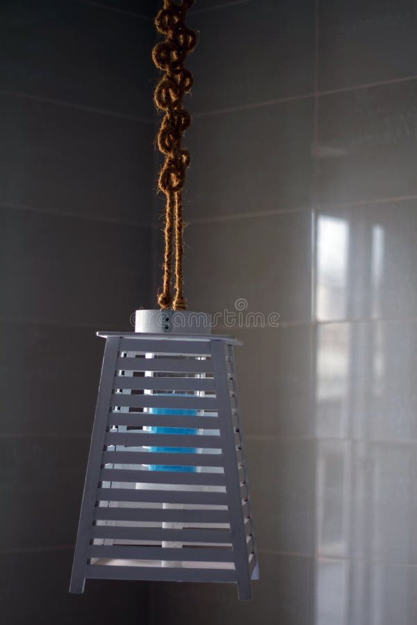 Lámpara azul hecha a mano, de tablas de madera y cuerda, contra una pared de baldosas claras, enfoque selectivo