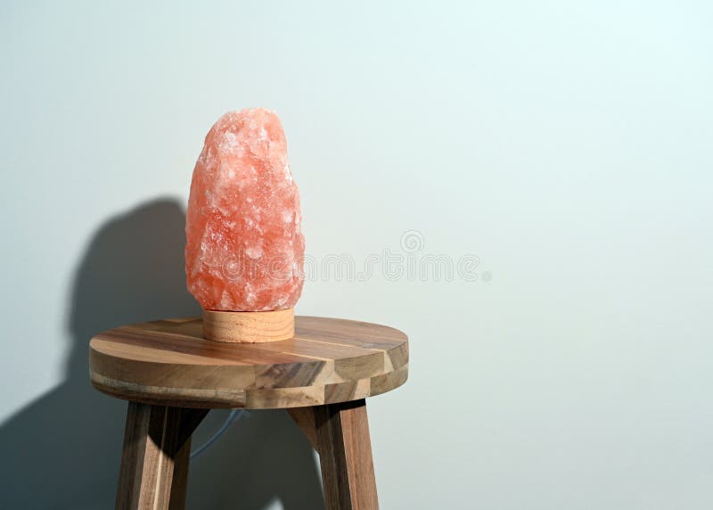 Lámpara de sal himalaya sobre una mesa de madera cerca de una pared neutra con espacio de copia