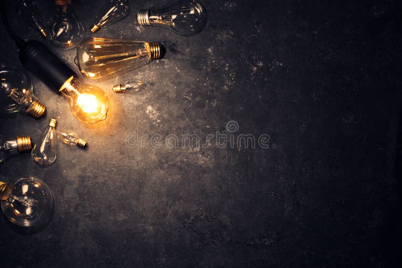 Lâmpada velha e vítrea brilhando sobre fundo escuro grosso cercado por lâmpadas queimadas Ideia, conceito de criatividade