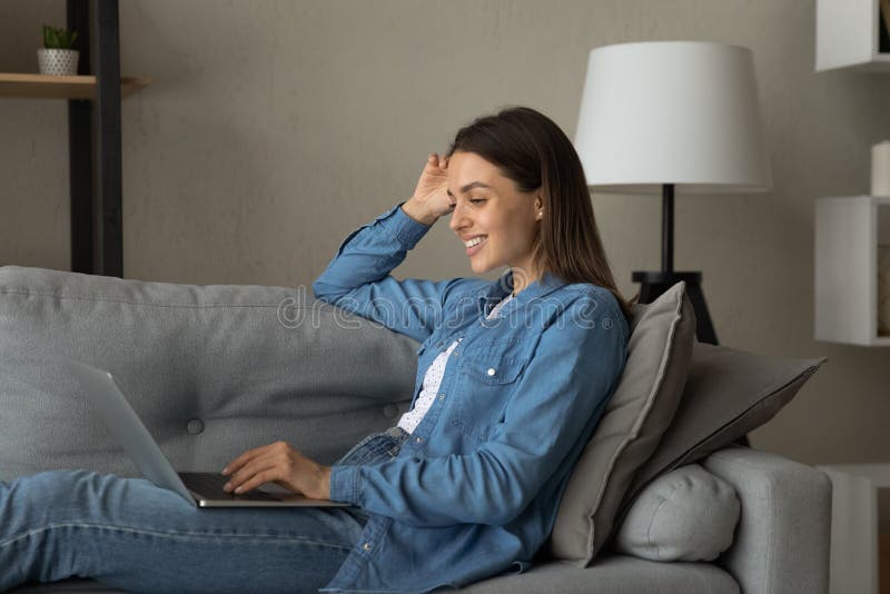 Lächeln Frau der Datenzugriffsseiten-Ansicht mithilfe des Notebooks auf der Couch sitzt lizenzfreie stockfotografie