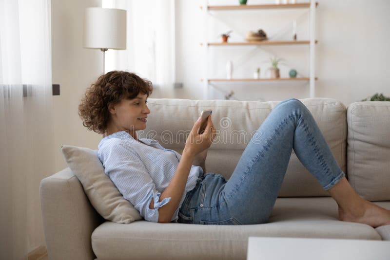 Lächeln junge Frau der Datenzugriffsseiten-Ansicht, die sich zu Hause mit Telefon gelockert stockfotos