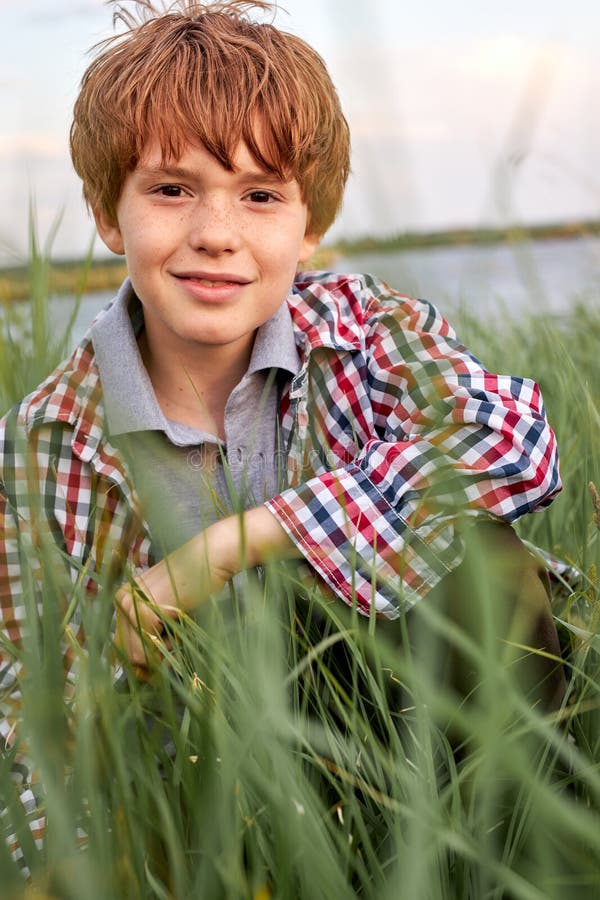 Lächelnd junge gut aussehende Teenager-Junge in casual kariert Hemd sitzen im Gras gekleidet