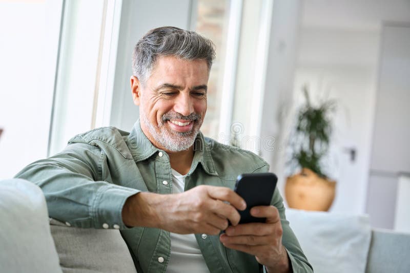 Lächelnd reifer Mann mittleren Alters mit Mobiltelefon sitzend zu Hause auf Couch. lizenzfreies stockbild