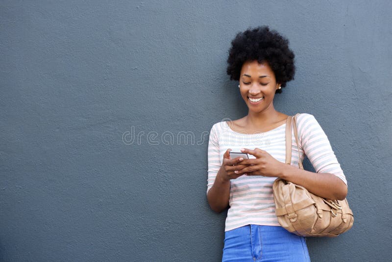 Lächelnde afrikanische Frau mit der Tasche, die Handy betrachtet