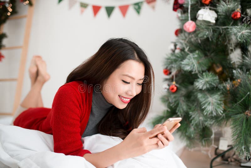 Lächelnde asiatische Frau der Junge benutzt Handy Weihnachten und N stockfoto Lächelnde asiatische Frau der Junge benutzt Handy Weihnachten und N stockfoto