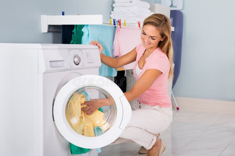Lächelnde Frau, die Kleidung in Waschmaschine einsetzt stockfotos