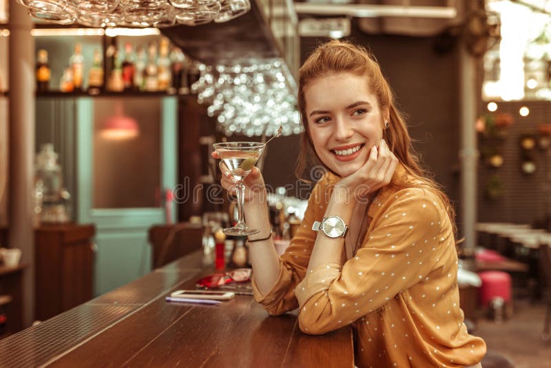 Lächelnde Frau, die Martini-Getränk sitzt am Barzähler hält lizenzfreie stockbilder Lächelnde Frau, die Martini-Getränk sitzt am Barzähler hält lizenzfreie stockbilder