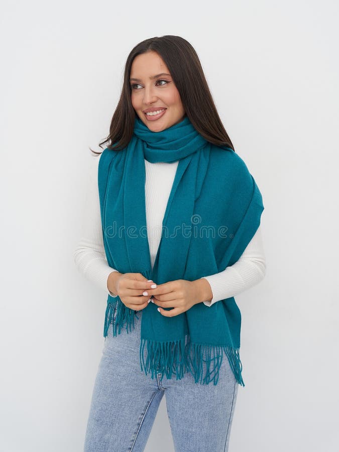 Lächelnde Frau mit langen dunklen Haaren mit türkisfarbenem Schal und weißem Pullover. Sie steht gegen eine weiße Mauer lizenzfreie stockbilder
