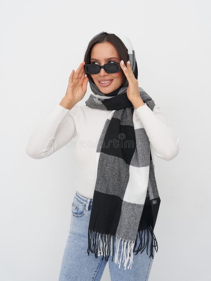 Lächelnde Frau mit Sonnenbrille und Schal mit Schachbrett in weißem Pullover und blauer Jeans. Ihre Hände passen die stockbild