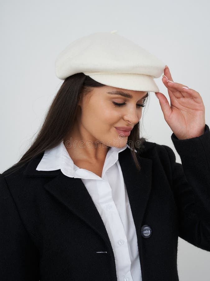 Lächelnde Frau mit weißer Beete und schwarzem Mantel, die ihren Hut berühren. Die Frau hat langes dunkles Haar und trägt ein Weiß stockbild