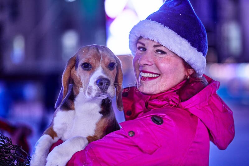 Smiling middle-aged woman in Santa Claus hat on a night walk with her puppy. Close-up. Smiling middle-aged woman in Santa Claus hat on a night walk with her puppy. Close-up